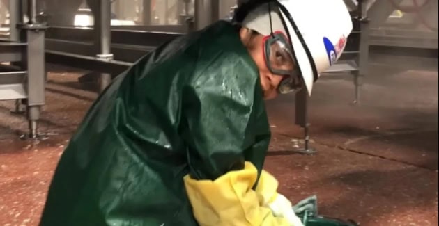 Young person in full workwear, including protective hat, googles, rubber gloves and waterproof coat crouching on the floor